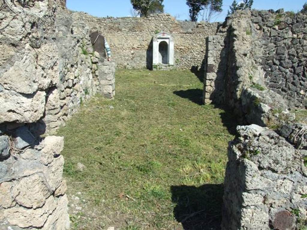 I.2.17 Pompeii. March 2009.  Doorway into room 12, oecus, looking east to doorway into room 13, peristyle garden.  Warscher writing in her Codex, quoting Mau in Bull. Inst. 1874, p.265, described this as –  “Passiamo adesso nel peristilio, accessibile per la seconda camera a sinistra dell’atrio. E desso piuttosto spazioso ed ha portici verso N e O, il cui tetto era sorretto da due pilastri messi insieme, sull’angolo, ed un’altro sul lato di N, ma più verso E, per lasciar libero lo sguardo dal triclinio situato da quella parte. Verso S e E il muro del giardino è diviso in scompartimenti intermediati da altri stretti, in ciascun de’quali è dipinto un candelabro.  Invece gli scompartimenti grandi sono riempiti della pittura d’un giardino: un cancello, sormontato in ciascun scompartimento da un’anfora, e dietro di esso un boschetto con uccelli: a destra e a sinistra Ibis e nel mezzo un faggiano. 
I portici ed i pilastri hanno una decorazione semplici: senza zoccolo vi sono scompartimenti rossi alternativamente stretti e larghi, alti m. 1,46 divisi da striascie gialle e contornati da linee bianche.  Quegli stretti sono abbelliti d’una ghirlanda verticale, mentre fra que’larghi su due troviamo una ghirlanda attaccata colle due estremità, sul resto qualche animale come uccelli ecc”.
See Warscher T., 1935. Codex Topographicus Pompeianus: Regio I.2. (no.31), Rome: DAIR, whose copyright it remains.
(translation: “We go now to the peristyle, accessible by the second room on the left of the atrium. It was rather spacious and had porticoes towards the north and west, whose roof was supported by two pillars linked together on the corner, and another on the north side, but more towards the east, to leave free the view from the triclinium situated at that part. Towards the south and east, the wall of the garden was divided into compartments, between which were narrow ones, in each of which a candelabra was painted. The large compartments instead were filled with a painting of a garden: a gate, surmounted in each compartment by an amphora, and behind it a wood with birds: Ibis were to the right and to the left, and in the middle a pheasant. The porticoes and pilasters had a simple decoration: without a zoccolo, there were red alternately narrow and wide compartments, 1,46m high,  divided by yellow stripes and surrounded by white lines. The narrow ones were embellished with a vertical garland, while between those wide on two were found a garland attached with the two ends, on the rest some animals, like birds, etc.”)