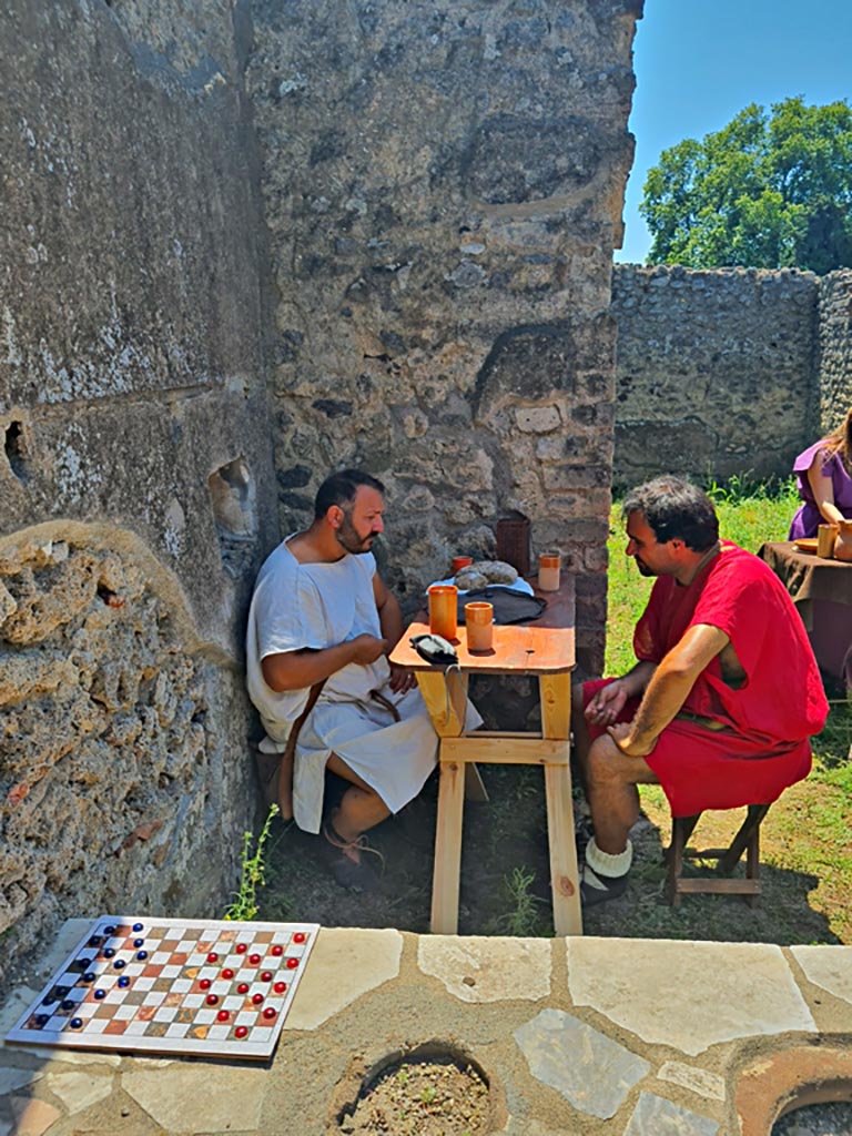 I.2.18 Pompeii. 8th June 2024. 
Looking south across counter with actors playing part of customers. Photo courtesy of Giuseppe Ciaramella.
Historical reconstruction entitled L’altra Pompei prende vita (The other Pompeii comes to life).