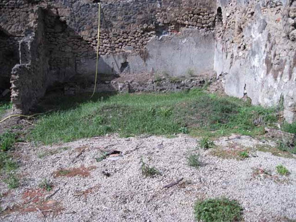I.2.24 Pompeii. September 2010. 
Looking north across site of summer triclinium and peristyle, from south portico. Photo courtesy of Drew Baker.
According to Jashemski, this Caupona or Officina Libraria had a portico on the south and east sides of the garden area.
The columns were connected by a low wall with an entrance to the garden on the west.
The caupona was excavated in 1873. There was a masonry triclinium with a table in the garden.
Two large breaks in the triclinium, which is today badly damaged, reveal the amphorae used in its construction.
Fiorelli believed that the low podium along the north wall held pots of flowers.
Mau reported a drainage channel at the corner of the triclinium, but it is no longer visible.
Only the base of an aedicula lararium built against the east wall opposite the north end of the east couch can still be seen.
See Jashemski, W. F., 1993. The Gardens of Pompeii, Volume II: Appendices. New York: Caratzas. (p.25)
According to Boyce, in the east wall of the peristyle, above one of the beds of a masonry triclinium was a niche.
It was described by Fiorelli as a sacrario.
More fully described by Mau as an “aedicula, una base, con una piccola tavola, che sta in una specie di nicchia coperta a volta, e probabilmente conteneva un’idolo”.
There remains now only the solid base, (0.40 by 0.32, h.0.65) and on the wall above it, the marks left by a vaulted structure which rested on the base.
Bull. Inst, 1874, 262; Fiorelli, Descr., 47.
See Boyce G. K., 1937. Corpus of the Lararia of Pompeii. Rome: MAAR 14. (p.23, no.17) 
As this book was written in the 1930s, it is probable that there is now even less evidence of the niche, following the bombing in the near vicinity in 1943, and the damage of the 1980 earthquake.
Possibly the solid base may be visible on the extreme right of the above photo, but would need a clearer photo.
If the white lapilli is covering the site of the triclinium, then the stone in the photo would seem to be in the correct place, “against the east wall opposite the north end of the east couch”, but according to Boyce’s measurements appears to look too small.