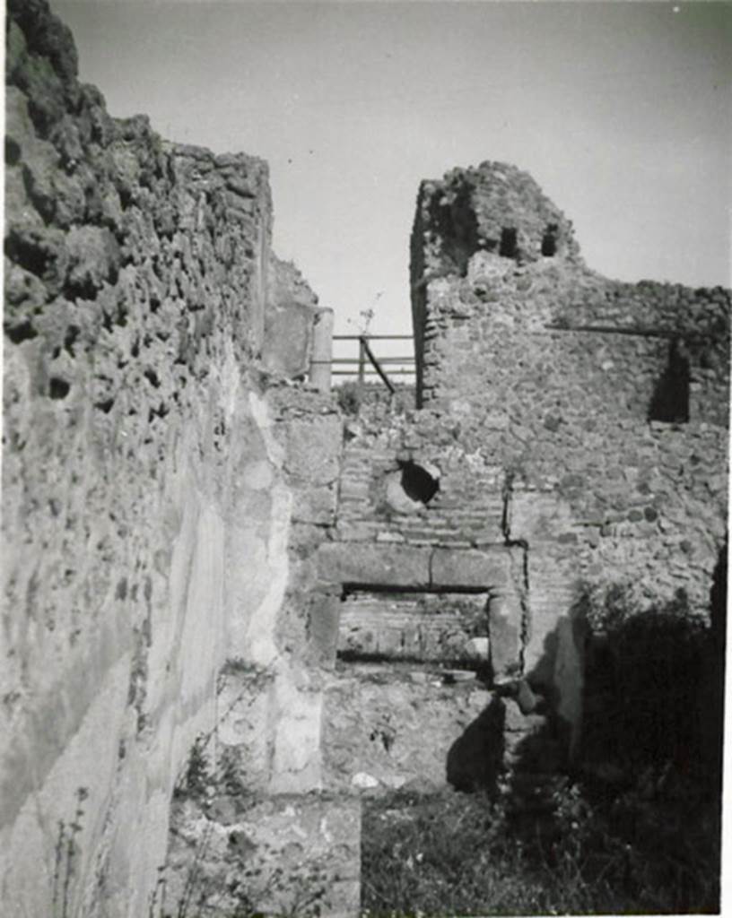 I.3.1 Pompeii. 1935 photograph taken by Tatiana Warscher.
Looking towards oven in north-east corner.
According to Warscher, quoting Fiorelli,  “1.3.1. Officina di un pistor dulcarius, che nella taberna prospiciente la via esposti i prodotti lavorati nell’attigua cella, la quale prendeva lume dalla bottega, avendone altra più rozza alle spalle, ed a cui si perveniva passando innanzi al forno; una scala di legno poggiata al muro, ch’è a sinistra della porta, menava alle stanze superiori. Nel foro per il fumo dello forno è incastrata una cornice di terracotta, forse semplicemente un pezzo di anfora. In fondo si vede il muro con fori di traverse della casa No. 3.
(translation: “A workshop of a sweet-pastry maker, that in the shop overlooking the roadway, displayed the products made in the adjacent room, which took its light from the shop, having another rustic room behind, and through which you passed to reach the oven; a wooden ladder rested against the wall, which is to the left of the door, leading to the upper rooms. In the smoke hole in the oven was embedded a terracotta cornice, perhaps simply a piece of amphora. At the rear you see the wall with holes of crossbeams of the house at I.3.3.”)
See Warscher T., 1935. Codex Topographicus Pompeianus: Regio I.3. (no.1), Rome: DAIR, whose copyright it remains.