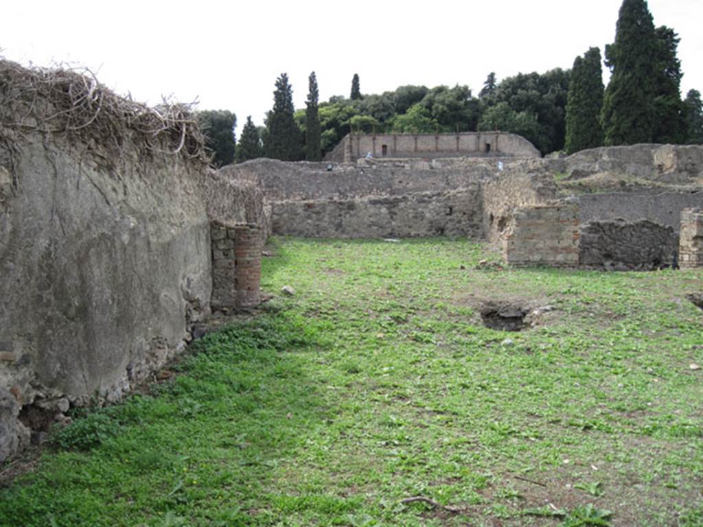 I.3.3 Pompeii. September 2010. Upper peristyle area, looking west towards the large exedra or triclinium, from the south-east corner. Photo courtesy of Drew Baker.
According to Warscher this was “triclinium “n”, south-west of the peristyle. She wrote –
“Nel pavimento cioè si vede un ornamento di forma quadrata, formato di pietruzze bianche, che non stando nel bel mezzo, ma più nell’interno della camera non poteva servir ad altra se non a segnar il posto ove fra letti si metteva la tavola.
Qui però non stavano che due letti, i cui posti bene si riconoscono dal pavimento meno consumato. Nel muro N e verso S vi sono fori per lasciar scolare l’acqua. Le pareti sono decorate in nero con ornamenti architettonici nel terzo stile di Pompei (Giorn.Sc II, p.452 segg). Il quadro che in parte distrutto vi si trova fu descritto da me e spiegato per Ippolito con la nutrice nel Bull. 1873, p.273. Poi seguiva verso N un corridoio obbliquo che dirigendosi verso l’atrium conduceva alle stanze superiori. Ma di questo corridoio nulla è rimasto: si riconosce soltante dalle buche de’ travi che lo sorreggevano…” (see photograph no.1, at I.3.1)
See Warscher, T, 1935: Codex Topographicus Pompejanus, Regio I, 3:  Rome, DAIR.  
(translation:  "In the floor one could see a square-shaped ornament that was formed from white stones, that were not in the beautiful middle, but more in the inside of the room where they could only serve as a sign to show the place where one put the table, between the couches. Here, however, there were only two beds, their place known well from the floor less worn.  In the north wall and towards the south, there were holes to let the water drain. The walls were decorated in black with architectural ornaments in the Third Style of Pompeii (Giorn.Sc II, p.452 following). The picture found here that was partly destroyed, was described by me and explained as Hippolytus with the nurse, in Bull. 1873, p. 273. Then followed towards the north, a sloping corridor that pointed towards the atrium leading to the upper rooms. But nothing remained of this corridor: one can recognize only the holes of the beams that supported it ... " (see photograph no.1, at I.3.1).