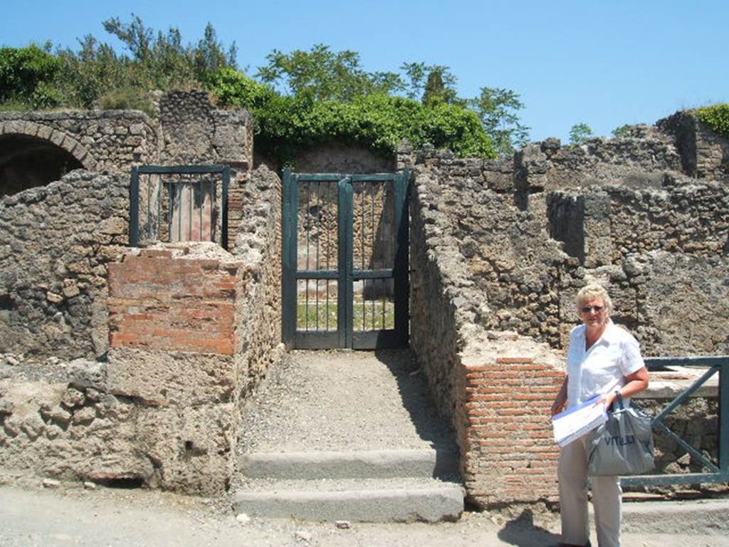 I.3.3 Pompeii. May 2005. Entrance on Via Stabiana. According to Warscher, quoting Bull. Inst, 1874, p. 183, she wrote –
Quanto alla pittura decorativa di questa casa, nella parte più bassa di essa tutte le pitture mostrano lo stile degli ultimi tempi di Pompei, coll’eccezione della camera a destra della scala. 
Ed alla stessa epoca di quella camera, la terza cioè fra quelle pompeiane, se non m’inganno, appartiene tutto quello che sta intorno al peristilio. Ho parlato appunto di questa casa nel Giorn. d Sc. II, p.456. Chiara è l’identita delle stile riguardo la prima camera dal suo lato occidentale. Il resto delle camere è decorato in uno stile che può dirsi quello de’candelabri, perchè divide la parete in tre parti mediante candelabri molto sottili e svelti. E come accennai nel luogo citato, appunto le pitture di queste camere mediante certe piccole particularità non tanto facili a descriversi ci fanno riconoscere questo stile come affine e probabilmente contemporaneo a quello delle due camere menzionate. Ed allo stile di queste pare appartenesse anche la decorazione del peristilio stesso, benchè poco ne sia conservato.
Que’ cambiamenti adunque che, come sopra accennai, subì la casa in discorso, si rileva dalla stessa decorazione che non ebbero luogo negli ultimi tempi di Pompei, ma probabilmente prima del terramoto dell’a. 63 d.C.
See Warscher, T, 1935: Codex Topographicus Pompejanus, Regio I, 3: (dopo no. 11a), Rome, DAIR.