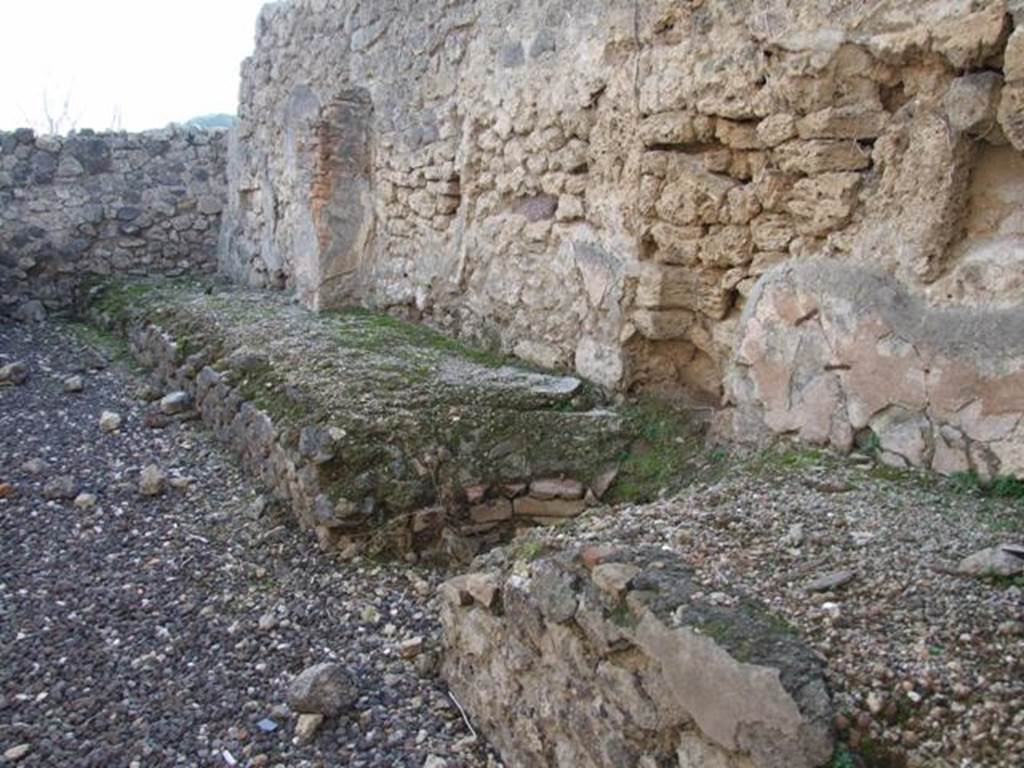 I.3.16 Pompeii. December 2007. West wall with remains of podium.  This used to have two tubs at the south end.  The boiler, the round gap in the centre of the picture, was used to heat a vessel.