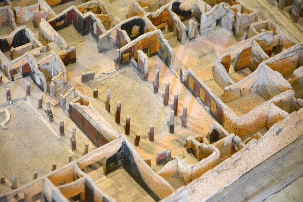 I.4.25 Pompeii. May 2019. Detail from model in Naples Archaeological Museum. 
Looking north-west across upper peristyle 56, in centre, towards open doorway into atrium 47, and through to entrance on Via dell’Abbondanza, centre top.
Foto Tobias Busen, ERC Grant 681269 DÉCOR.
According to Jashemski –
The north (Upper) peristyle garden, which belonged originally to a house whose entrance was on the Via dell’Abbondanza, was reached by a flight of steps from the central (Middle) peristyle which lies on a level about two metres below. This (Upper) garden was surrounded by a portico on the south, east and most of the north sides. There was a travertine puteal between the two middle columns on the east side. On the west, a large exedra (room 57), preceded by a vestibule, had a splendid view of the garden, as did the triclinium (room 58) on the east. The columns, like those in the central peristyle, were made of brick and Sarno limestone and faced with stucco. The columns, with the exception of those opposite the entrances of the large exedra, the triclinium, and to the atrium on the north, were left unfluted. There was a gutter around the edges of the garden.
See Jashemski, W. F., 1993. The Gardens of Pompeii, Volume II: Appendices. New York: Caratzas. (p.31-32).