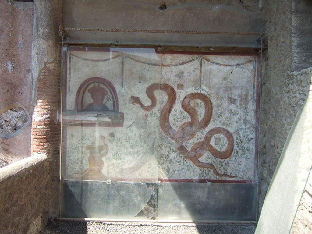 I.6.2 Pompeii. May 2006.  Painted lararium on west wall near portico.  
Fortunately, the lararium was not damaged by the bombing of 19th September 1943, whereas the nearby portico was destroyed.
According to Boyce, above a black dado there was a white panel marked off by red stripes. On the left side was an arched niche with a projecting ledge beneath it. The bust of Mercury was painted on the rear wall of the niche. On the right side of the white panel there was a large yellow serpent, raising his head to the niche.  Below the niche was a second serpent coiling around a yellow cylindrical altar. There were painted green plants with red, yellow and blue flowers, amongst them were two butterflies and three birds. Near the larger serpent there was a peacock standing amongst the plants. Across the top, there were three garlands.
See Boyce G. K., 1937. Corpus of the Lararia of Pompeii. Rome: MAAR 14. (p.25, no.36, pl.9,3)