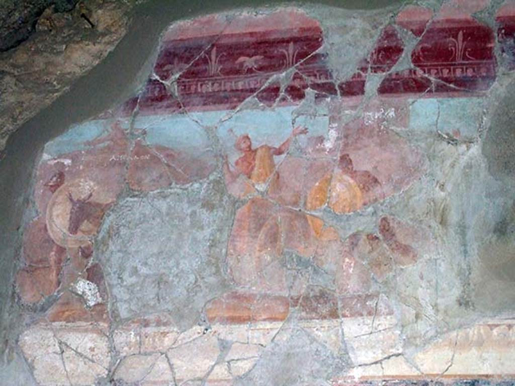 I.6.2 Pompeii. May 2006. Detail of wall painting from west wall of the western wing of the cryptoporticus.
According to Peters, this was known as “the pestilence scene”, and was reconstructed from fragments.
Apollo can be seen with his bow, firing the plague arrows, above the rocks, in the upper left. 
The name of the god had been written on the painting in Greek letters (in white below the figure). 
People from Achaea pass in the foreground, including a man in a wagon drawn by a donkey, followed by man with a large round shield.
See Peters, W.J.T. (1963): Landscape in Romano-Campanian Mural Paintings. The Netherland, Van Gorcum & Comp.   (p.23 and fig.12)