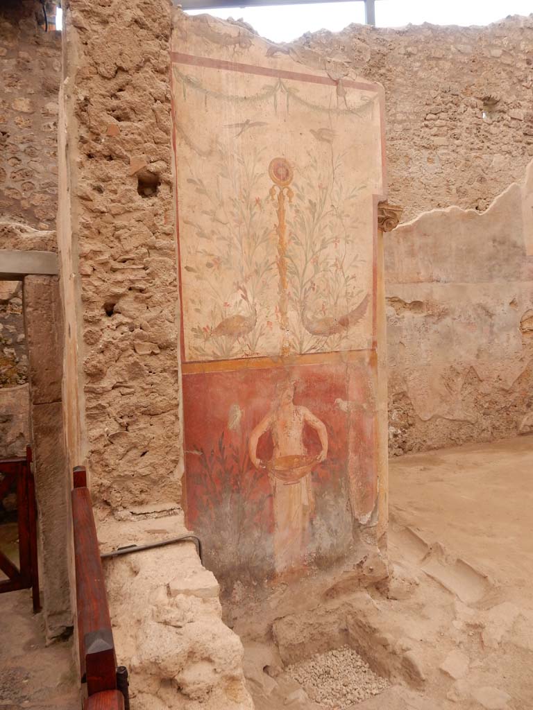 I.6.15 Pompeii. June 2019. Room 9, small garden. 
Wall on west side with painting with birds, plants and a medallion above a figure holding a basin or bowl.
Photo courtesy of Buzz Ferebee.