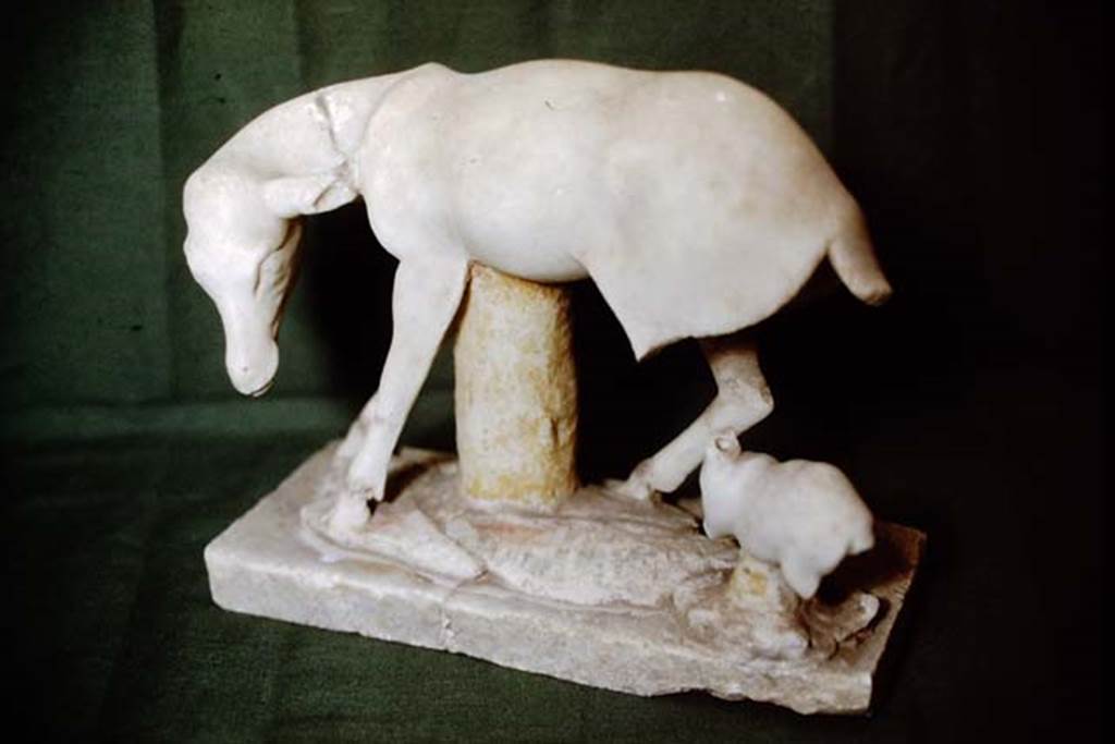 I.7.11 Pompeii, 1978. Statuette of a deer suckling a young faun. Photo by Stanley A. Jashemski.   
Source: The Wilhelmina and Stanley A. Jashemski archive in the University of Maryland Library, Special Collections (See collection page) and made available under the Creative Commons Attribution-Non Commercial License v.4. See Licence and use details. J78f0096
This broken statuette was also made of very fine marble and had been gilded. Two other statuettes were also found in the triclinium, one was a headless statue of a white marble satyr, extremely drunk and stretched out on a rock of grey marble. Of the other, only a base of grey marble imitating rocky terrain and showing the goat feet of Pan on a white marble base was found.