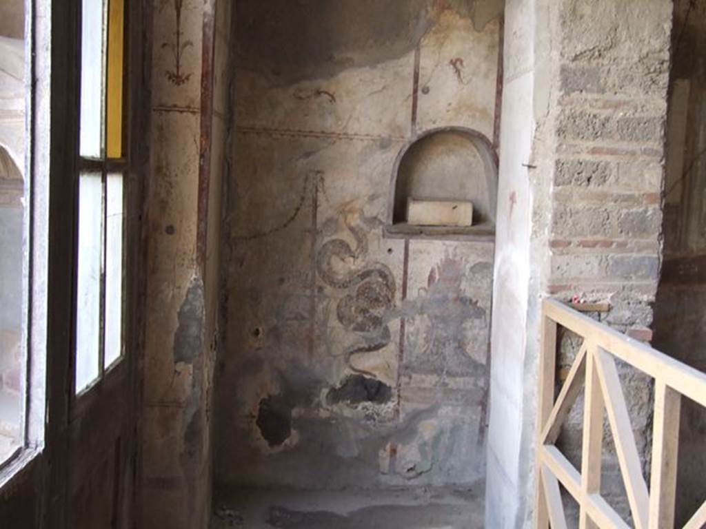 I.7.11 Pompeii. December 2006. Lararium on west wall. According to Boyce, in a very narrow room opening off the north-west corner of the peristyle and west of the triclinium is a lararium. The arched niche is simply decorated with a dark stripe outlining the niche against the white of the surrounding wall. On the wall below the niche are two painted serpents, one on each side. Their heads are on a level with the floor of the niche.  (Boyce then gives a note that these serpents direct their heads to the niche as if to receive the offerings placed in it, rather than to the offerings on the burning altar). The serpent on the left is larger and has a red crest and beard, the other serpent being smaller, with neither crest or beard. Between the serpents, under the niche, is a painted flaming altar in the form of a metal brazier. On top of the brazier are eggs. Plants are in the background, and stylized candelabra with festoons border the painting on the sides. Not. Scavi, 1927, 52 with photograph. See Boyce G. K., 1937. Corpus of the Lararia of Pompeii. Rome: MAAR 14. (p.26, no.41B)