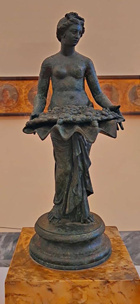 I.7.12 Pompeii. October 2023. 
Bronze statuette of Pomona. Photo courtesy of Giuseppe Ciaramella. 
On display in “L’altra MANN” exhibition, October 2023, at Naples Archaeological Museum.
According to Jashemski, this statue can be seen in her photo on p.39, fig.38, inv. 144276.
See Jashemski, W. F., 1993. The Gardens of Pompeii, Volume II: Appendices. New York: Caratzas, (p.38).
According to Naples Museum –
“This bronze statue, with another of a bathing Aphrodite, was described as Bathing Aphrodite with Nymphs, inv. S.N.”
The description card described the group as from the Vesuvian area, as opposed to I.7.12, Pompeii.
So the bronze statue may, or may not, come from I.7.12.