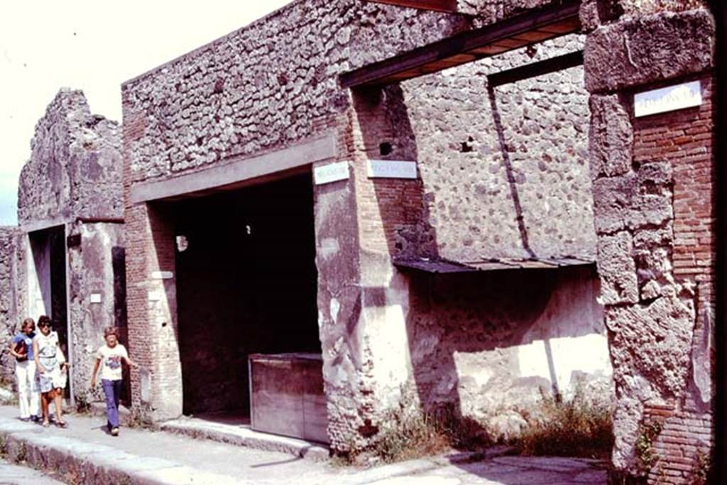 I.8.1 Pompeii. 1976. Looking south-east towards entrance to shop, and east wall of small vicolo with remains of painted street shrine.  Photo by Stanley A. Jashemski.   
Source: The Wilhelmina and Stanley A. Jashemski archive in the University of Maryland Library, Special Collections (See collection page) and made available under the Creative Commons Attribution-Non Commercial License v.4. See Licence and use details. J76f0355