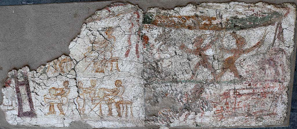 I.8.10 Pompeii. December 2018. Paintings found to the east of the entrance façade.
One of two paintings on the façade showed Mercury with a group of men attired in costumes resembling those of the later Neapolitan Punch and Judy puppets.
The second shows men seated at tables on which are a variety of vases, possibly indicating a taberna vasaria selling vases.
PAP inventory number 45622.