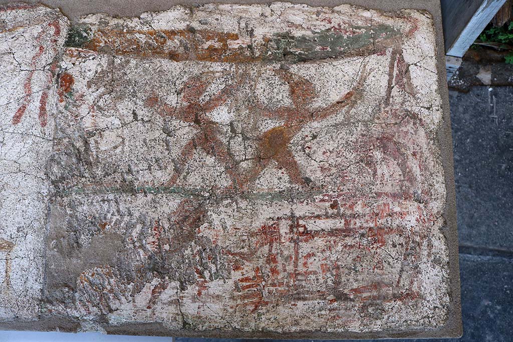 I.8.10 Pompeii. December 2018. Entrance façade painting. 
Mercury with a group of men attired in costumes resembling those of the later Neapolitan Punch and Judy puppets.
This led Della Corte to name this as the Hospitium dei Pulcinella.
PAP inventory number 45622.
According to Fröhlich, 
The figures are dark brown, reddish and light red, the dividing line between the two zones is green, the garland at the top of the picture is green and yellow.
The centre of the upper part of the picture is taken up by two dancing figures, each dressed in an apron and a pointed hat, who stride apart with wide steps, bending their upper bodies forward, spreading their arms wide and holding crossed sticks in each hand. On the left edge of the image is a white-robed figure with a donkey's head, on the right edge a horse or an ox, of which only the hind legs have survived. 
In the lower part of the picture, a small figure with a disproportionately large head appears to the right of a table on which a vessel is standing. On the right, a frame stands on four thin legs, from which the legs seem to hang down, perhaps a ferculum.
See Fröhlich, T., 1991. Lararien und Fassadenbilder in den Vesuvstädten. Mainz: von Zabern. (F5, p.307).