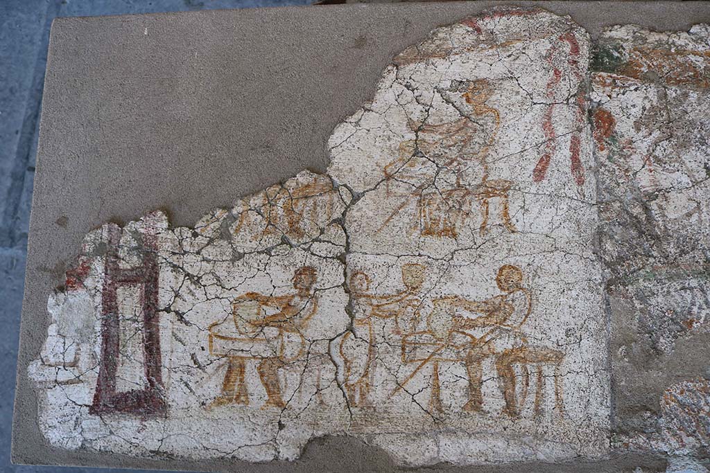 I.8.10 Pompeii. December 2018. Entrance façade painting. 
This shows men seated at tables on which are a variety of vases, possibly indicating a taberna vasaria selling vases.
PAP inventory number 45622.
According to Fröhlich, 
On the left edge, preserved only in the lower part, stands a female deity in long, belted robe with purple edges, probably Minerva. On her right is a round altar covered with burning sacrifices.
The four men are probably potters shaping vessels on one-legged wheels.
Lower right a female customer is examining two vases. Upper right are the remains of a garland.
See Fröhlich, T., 1991. Lararien und Fassadenbilder in den Vesuvstädten. Mainz: von Zabern. (F5, p.307).