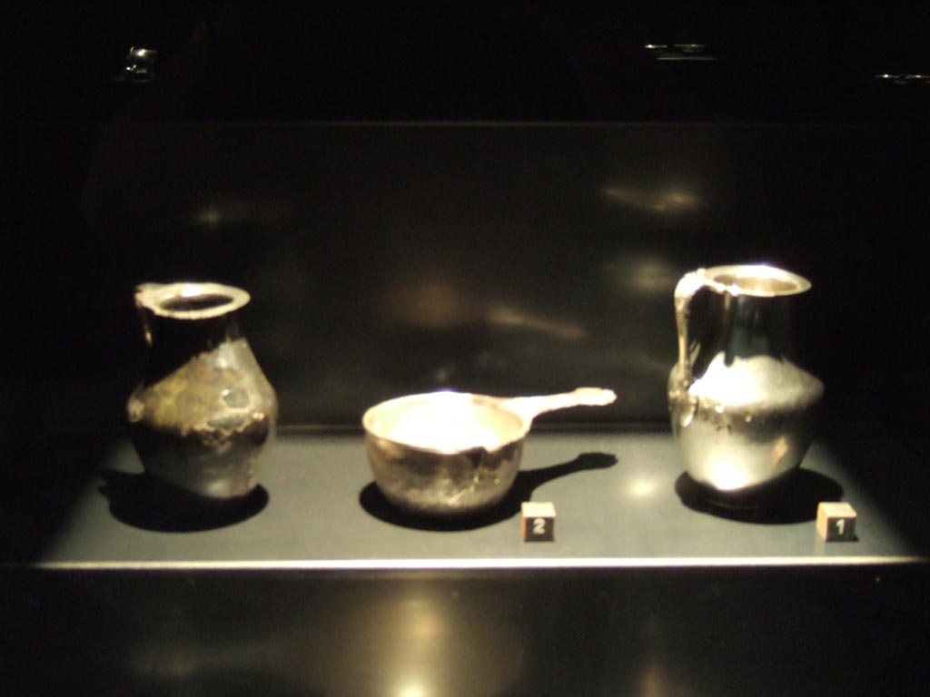 I.8.14 Pompeii. Silver found in the vestibule, probably kept in a wooden box. 
Jug - SAP inventory number 7478, a patera - SAP inventory number 7482 and jug - SAP inventory number 7477.
See Guzzo, P. (A cura di), 2006. Argenti a Pompei. Milano, Electa. (p. 148 and 150).