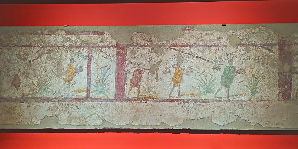 I.8.15 Pompeii. March 2024. 
Scene of a sacrificial procession, with figures in short tunics with graffitoed names near their heads, (61-79 AD).
On display in exhibition in Palaestra, entitled - “L’altra Pompei, vite comuni all’ombra del Vesuvio”. Photo courtesy of Giuseppe Ciaramella.