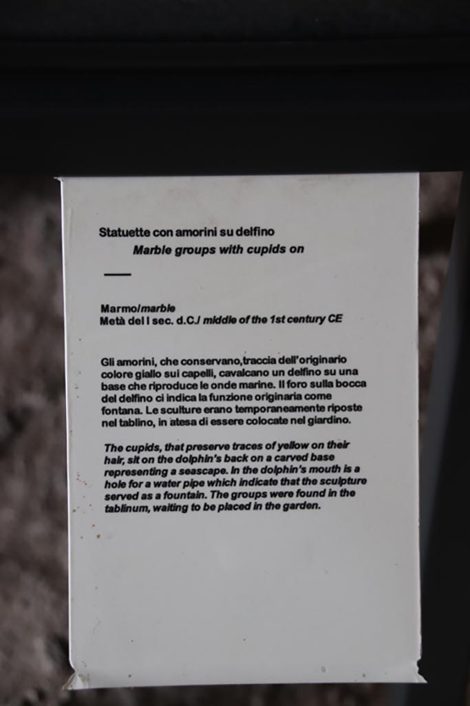 I.9.14 Pompeii. October 2022. 
Room 5, descriptive card for cupids on display in room 5, described as being found in tablinum, our room 6. 
Photo courtesy of Klaus Heese.
According to PPM – 
“from the sketch of the statuettes made at the time of excavation, it would seem that they were found on the floor of the atrium.”
See Carratelli, G. P., 1990-2003. Pompei: Pitture e Mosaici. Roma: Istituto della enciclopedia italiana, p. 173.