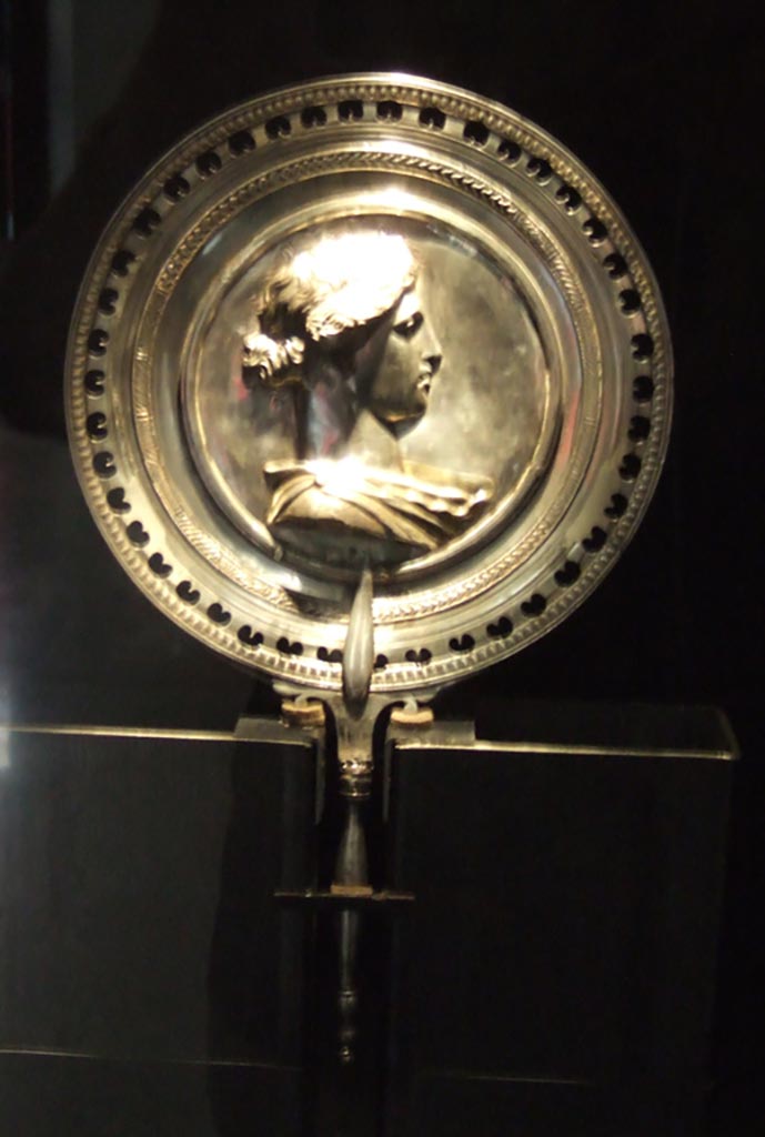 I.10.4 Pompeii. Richly decorated silver mirror with the bust of young woman in the centre. 
Part of the 115 pieces of Silver found in a chest in the underground storerooms. 
Now in Naples Archaeological Museum. Inventory number 145525.
See Guzzo, P. (A cura di), 2006. Argenti a Pompei. Milano, Electa. p.223.