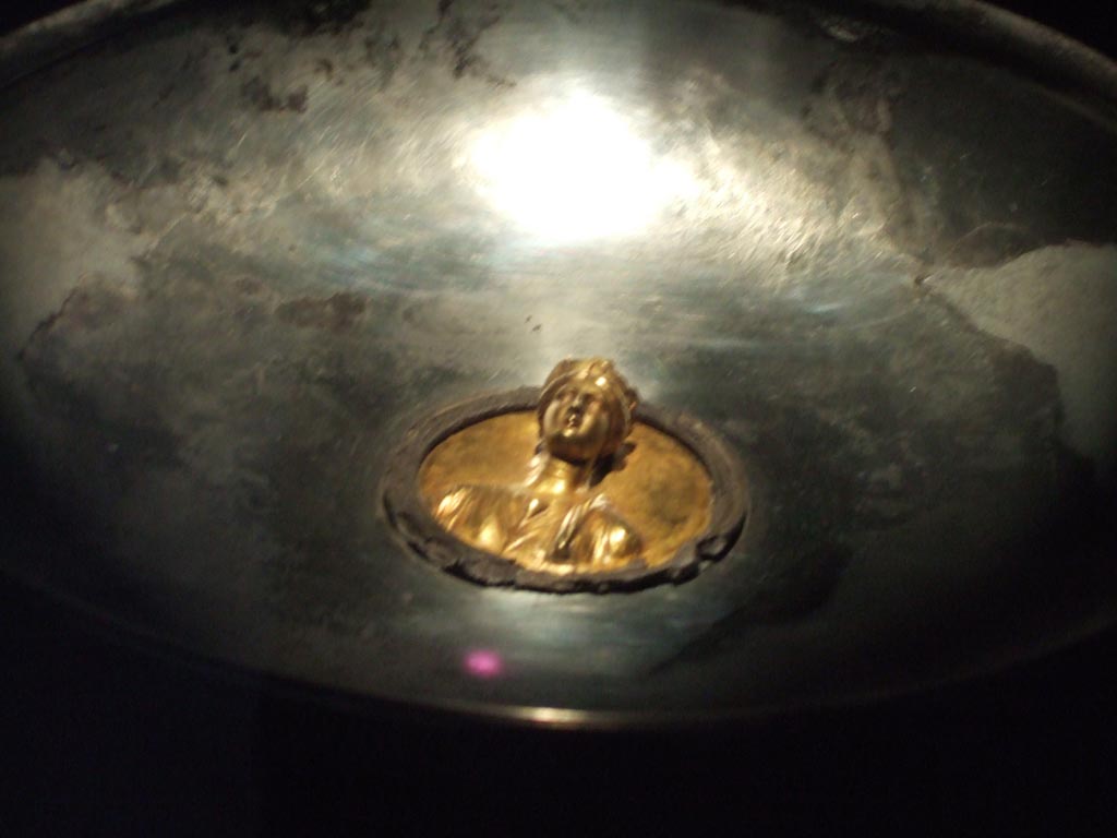 I.10.4 Pompeii. Gold bust of a woman in centre of silver phiale. 
On her head is a crown with walls, turrets and city gates, indicating the personification of a city.
Part of the 115 pieces of Silver found in a chest in the underground storerooms. 
See Guzzo, P. (A cura di), 2006. Argenti a Pompei. Milano, Electa. p.221.
