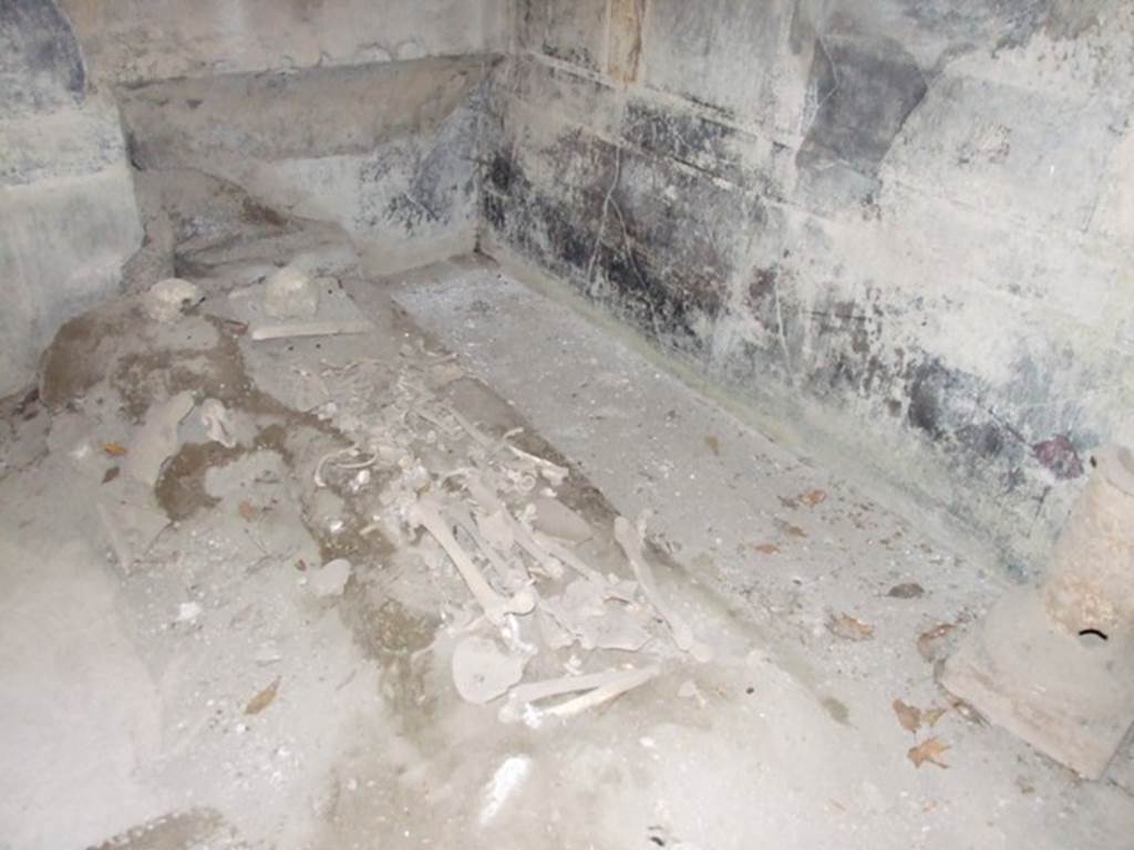 I.10.7 Pompeii. March 2009. Room 12, north-west corner of triclinium, with remains of skeletons. According to Civale, “in the triclinium two people had sought refuge: an adult who was discovered on the floor, his arms clutching the edge of a dining couch, and a second, younger victim his arms folded under the head and legs stretched out on the floor.  
On the ground between the adult’s feet, lay a little cloth bag containing a small hoard of 26 silver coins, amounting to just 104 sesterces.  
In the triclinium, another little heap of 48 coins was found, perhaps also the savings of one of the victims.” See Guzzo, P.G. ed. (2003): Tales from an eruption – (Civale, A: The House of the Craftsman). Milan, Electa; (p.140-41)