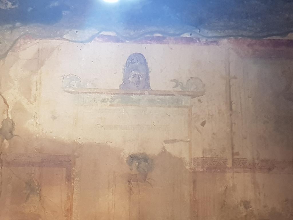 I.10.11 Pompeii. October 2022. Room 9, detail from upper west wall of painted mask and dophins. Photo courtesy of Klaus Heese.