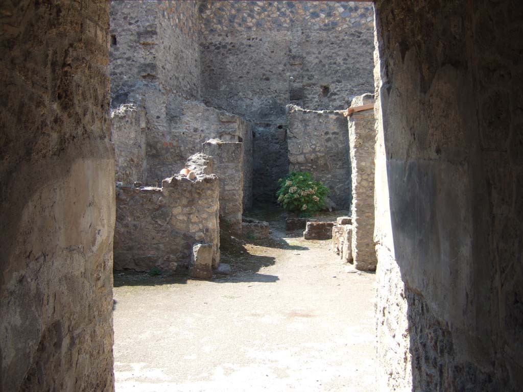 I.10.18 Pompeii. September 2005. Looking west from entrance fauces into atrium.
“The atrium, of an irregular shape, and paved with simple beaten-earth, had an impluvium of masonry (1.2m x 0.9m) faced with cocciopesto and embedded in its base were fragments of coloured marble, and this was placed almost in the middle of the atrium, but not in line with the entrance fauces. 
A high black zoccolo, followed by the rest of the walls simply painted white, without any decorations, was the uniform aspect of the walls on all four sides.”