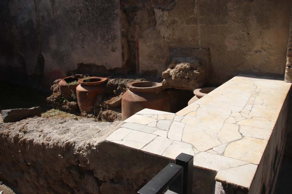 1.11.1 Pompeii. May 2015. Looking towards west side with remains of four urns and shelves for displaying drinking vessels.
Photo courtesy of Klaus Heese.