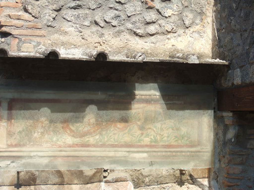 I.11.11 Pompeii. September 2005.  Lararium on north wall of thermopolium.
A stucco border surrounding a serpent moving left to a round altar.  In the background are green plants with red flowers. See Fröhlich, T., 1991. Lararien und Fassadenbilder in den Vesuvstädten. Mainz: von Zabern. (L21, T:14,1:24,2).