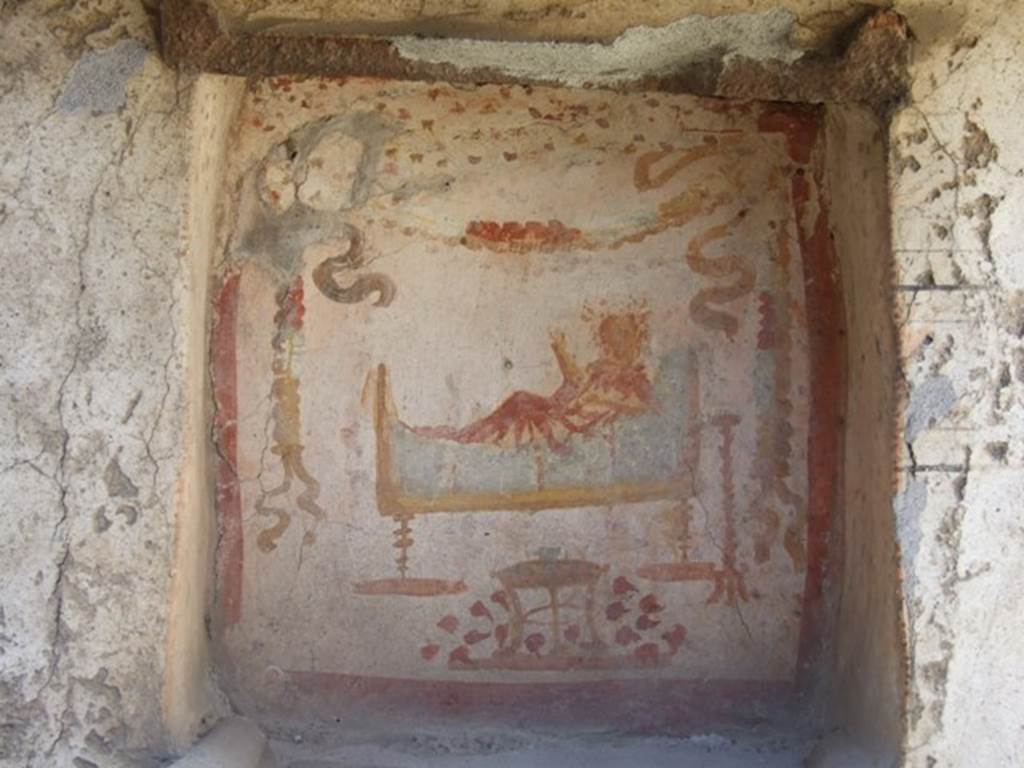 I.14.7 Pompeii. March 2009. West wall of garden area.  
Niche lararium with painting of a god in a long white robe lying on a couch.  
The right hand holds a branch and the left holds a patera.  
To the right is a golden candelabrum.  
At the front is a three legged table with a bowl of fruit.  Above is a garland.
See Fröhlich, T., 1991. Lararien und Fassadenbilder in den Vesuvstädten. Mainz: von Zabern. (L34, T:29,3)