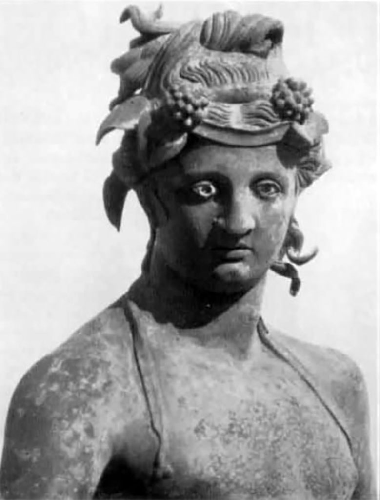 I.16.2, Pompeii. Detail of bronze statue of a young Bacchus.
See Elia, O., 1961. Bacco Fanciullo e Dioniso Chtonio a Pompei: Bollettino d’Arte 1961, Fasc. I-II, (p.2, fig.2). 
Kuivalainen comments –
This is another young Bacchus looking absentmindedly elsewhere, and not fully occupied with the activity he is engaged in.
He is pouring wine for a panther, and is perhaps intoxicated himself, as indicated by the position of his legs and the left hand, which once held a thyrsus tightly. The hairstyle may be inspired by Isiac counterparts. (489).
(Note 489 reads – Elia 1961, 2 – 3, suggested that the statue was a product of the eastern provinces).
See Kuivalainen, I., 2021. The Portrayal of Pompeian Bacchus. Commentationes Humanarum Litterarum 140. Helsinki: Finnish Society of Sciences and Letters, (H15, p.220).