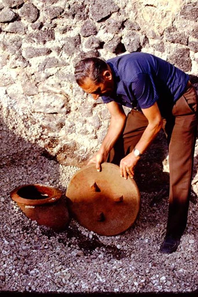 I.21.3 Pompeii. 1974. Removing the lid from the small dolium found buried near east wall. Photo by Stanley A. Jashemski.   
Source: The Wilhelmina and Stanley A. Jashemski archive in the University of Maryland Library, Special Collections (See collection page) and made available under the Creative Commons Attribution-Non Commercial License v.4. See Licence and use details. J74f0327