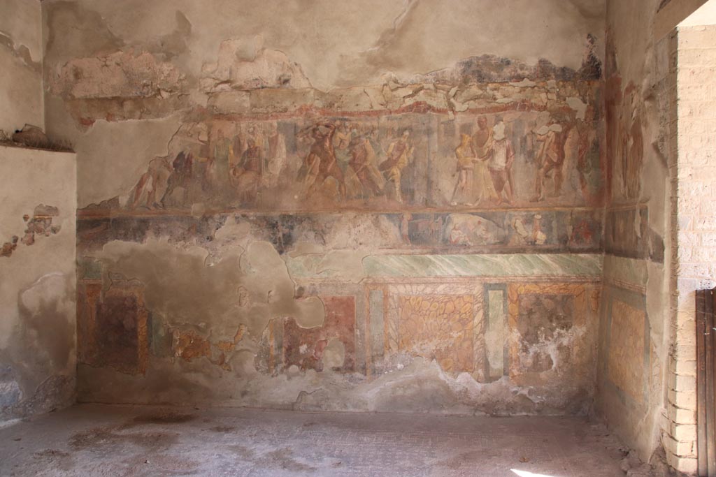 II.2.2 Pompeii. October 2022. Triclinium “h”, looking towards east wall. Photo courtesy of Klaus Heese
The larger upper section depicts three scenes
Telamon and Laomedon
Heracles and Laomedon, King of Troy and 
Hesione and Telamon.
The narrower lower section shows stories from the Trojan War featuring Achilles.
The Funeral of Patroclus.
Games in his honour.
Ransom of the body of Hector.