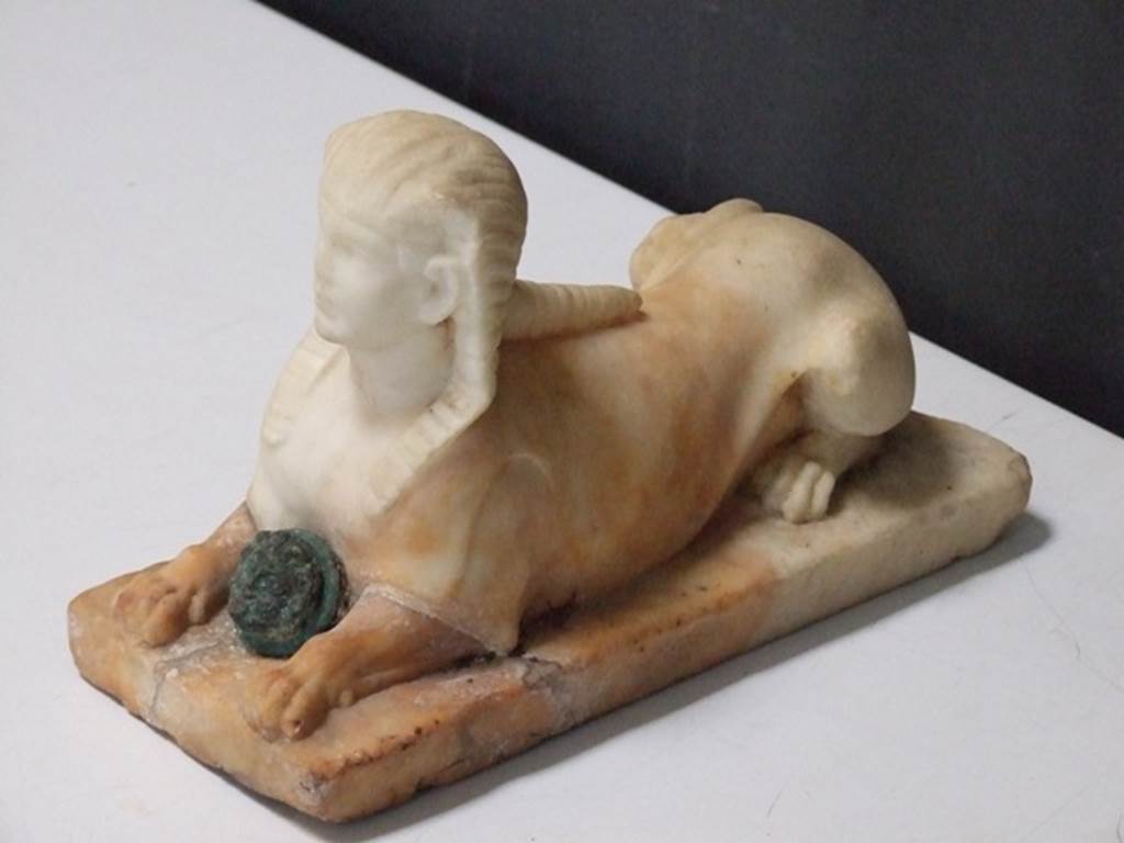 II.2.2 Pompeii.  March 2009. Room “i”. White marble statuette of Sphinx, with a face of a bronze gorgon between the front legs.  Found on the north side of the upper euripus in the garden in 1920.  SAP inventory number 2930.