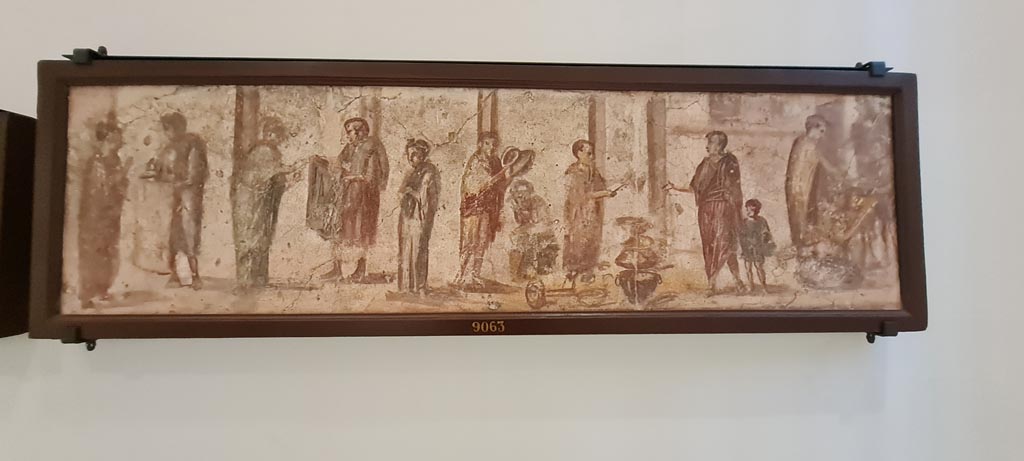II.4.3 Pompeii. April 2023. Paintings of the Forum frieze, on display in “Campania Romana” gallery in Naples Archaeological Museum.
Above (inv. 9063) – Vendita di tessuti, pentolame e pane davanti a colonnato. 
(Sale of fabrics, pots and pans and bread in front of a colonnade.)  Photo courtesy of Giuseppe Ciaramella.