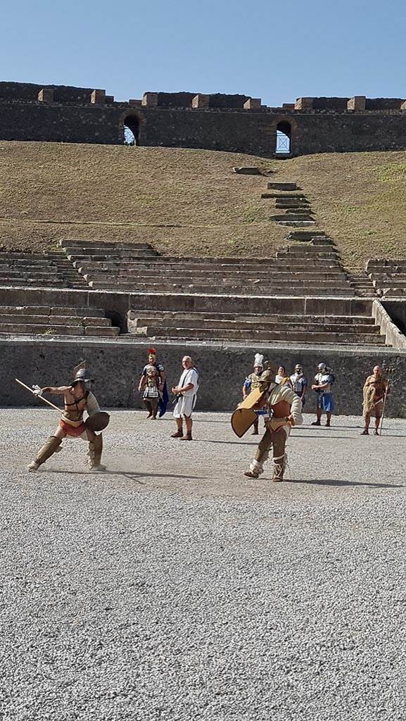 II.6 Pompeii. September 2024. 
Looking west across amphitheatre towards Gladiators in combat rehearsing.  
Photo courtesy of Giuseppe Ciaramella.