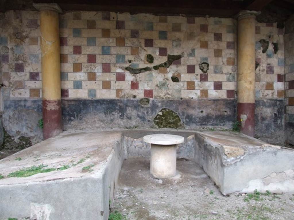 III.2.1 Pompeii. March 2009. Room 20, summer triclinium. Looking north.
According to Jashemski - “A portico supported by eight stuccoed columns, one of which was engaged, enclosed the garden on part of the west, south, and part of the east sides. The low wall built between the columns (which were white above the wall, and black below) was painted black and decorated with individual clumps of plants. A gutter outlined the east and south edges of the garden. There was an entrance to the garden from both the west and east porticoes. The rear wall of the garden had a vividly painted pattern made up of imitation marble cubes and rectangular blocks. Yellow, red and blue squares were painted in sequence between rectangles imitating white marble blocks with draughted margins and arranged so that each square fell in the middle of the rectangle below, thus producing a pattern of diagonals of squares of the same colour against a white background. Built against this colourful wall was the triclinium with couches of unequal length (l. medius, 4.62m; l. imus, 3.88m; l. summus, 3.27m., the latter with a fulcrum). Between the couches was a round table (yellow base, 0.40m in diameter; white marble top, 0.65m in diameter), with a jet which rose in the centre. 
Two sturdy stucco covered columns, red below and yellow above, stood at the edge of the couches at the back, as did two of the same king at the front.
The columns supported a pavilion, which Spinazzola thought must have been heavier than a simple pergola.
Food from the adjacent kitchen was probably passed through the window in the wall to the left of the triclinium; the niche on either side of the window would have been a convenient place to deposit things.”
See Jashemski, W. F., 1993. The Gardens of Pompeii, Volume II: Appendices. New York: Caratzas. (p.99)