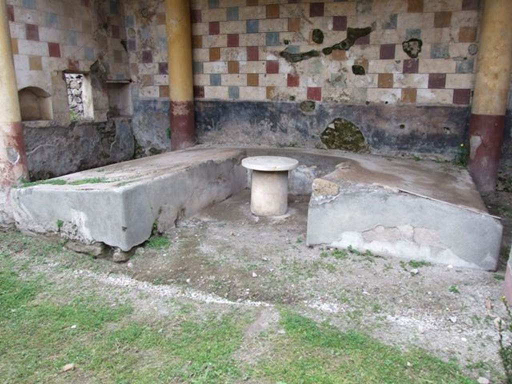 III.2.1 Pompeii. March 2009. 
Room 20, summer triclinium, showing couches of differing lengths, and two niches and window in west wall.
According to Soprano –
Ubicazione: peristilio. L. medius, m.4.50; l. imus, m.3.97; l. summus, m.3.97; diametro della mensa, m.0.40.
Bibliog. “Not.Scavi”, 1916, p.231: Maiuri, Pompei, p.68.
Al muro settentrionale del peristilio, decorato con una policroma decorazione a scacchiera, era addossato il triclinio in muratura. 
Quattro colonne doriche, rivestite d’intonaco giallo, sostengono una tettoia a spioventi destinata ad ombreggiare il triclinio.
Il solo l. summus ha il fulcrum.
La decorazione del triclinio, limitata sulle pareti esterne ad un semplice rivestimento in intonaco nero, conserva nelle pareti interne tracce di figurazioni: due grifi alati, araldicamente affrontati ai lati di un cratere (l. medius) e anitre pascenti tra piante, molto evanide (l. imus e summus).
La mensa circolare non presenta attualmente alcun rivestimento. (Note 1: Originariamente la mensa era ricoperta da un disco marmoreo (diam. m.0.65) rinvenuto al momento dello scavo.).
Per un rapido servizio nel trasporto dei cibi dall’attigua cucina serviva probabilmente la piccola finestra che si apre al centro della parete a sinistra del triclinio.
Egualmente a ripostiglio venivano adibite le due nicchie rettangolari ai lati della finestra.
See Soprano, P. (1950). I triclini all’aperto di Pompei. (In Pompeiana, raccolta di studi per il secondo centenario degli scavi di Pompei. Napoli, Gaetano Macchiaroli, Editore, P. 298, no.8).