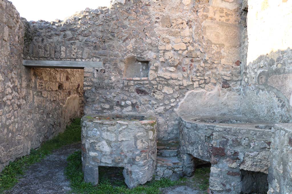 V.1.5 Pompeii. December 2018. 
Looking towards north wall with doorway to rear room and square niche/recess. Photo courtesy of Aude Durand.