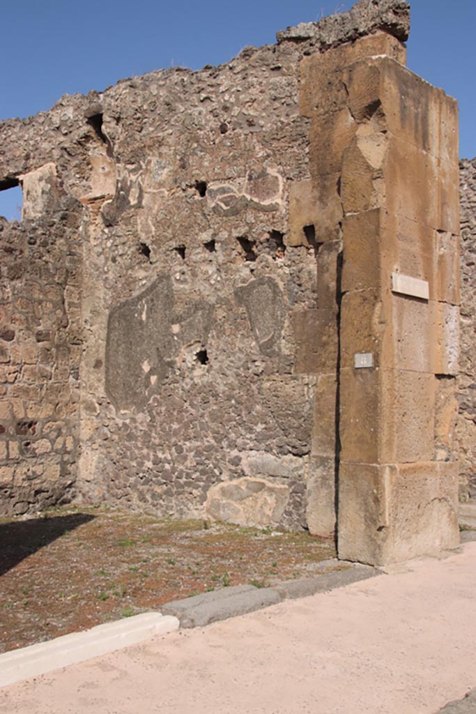 V.1.8 Pompeii. October 2023. 
East side of entrance doorway and east wall of shop-room. Photo courtesy of Klaus Heese.
An upper storey latrine can be seen in the upper north-east corner of the shop-room.