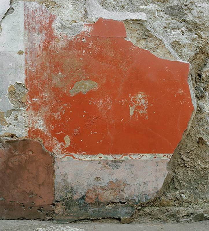 V.1.18 Pompeii. c.2005-2008.  
Room “l” (L), detail of painted decoration in centre of lower north wall. Photo by Hans Thorwid.
Photo courtesy of The Swedish Pompeii Project.
Under the central painting of Satyr and a Bacchante in the middle zone of the north wall, was a painted taut garland with head of Silenus and tambourine, in the centre of the red panel.