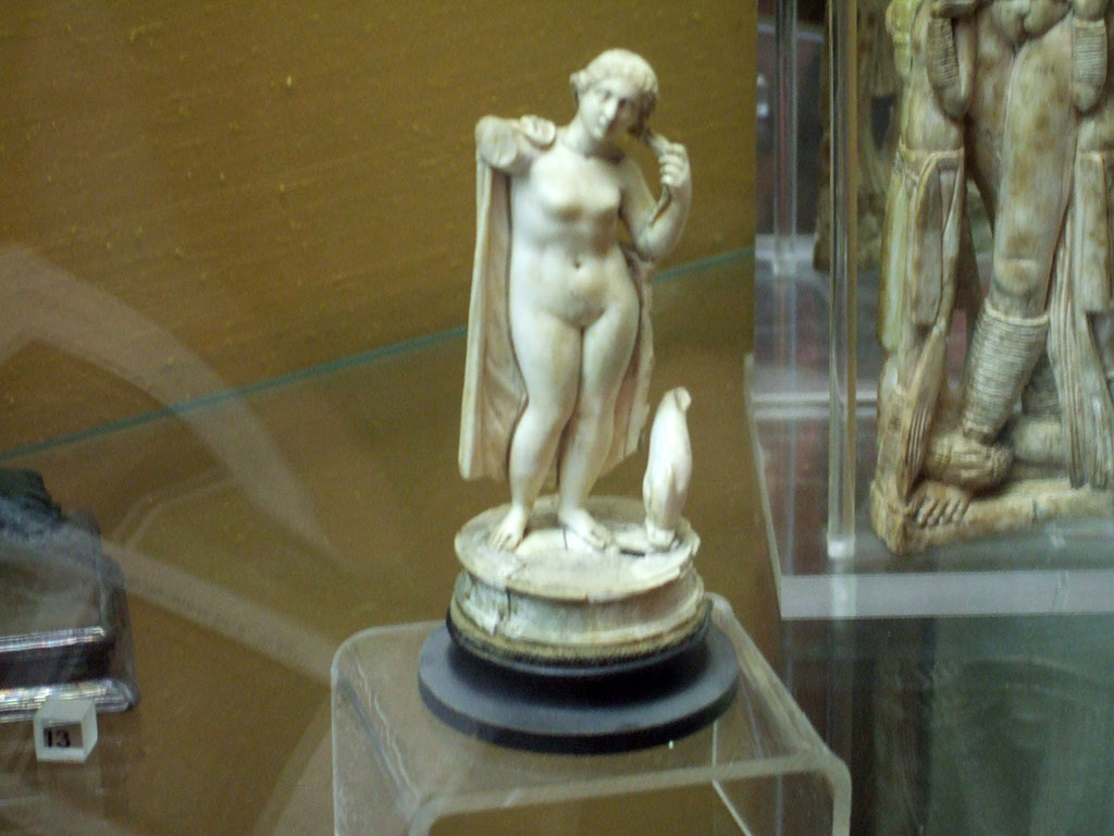 Ivory statuette of Venus Anadyomene with dolphin found in V.1.18 Pompeii.  
Now in Naples Archaeological Museum.  Inventory number 110924.
According to the note in Boyce, two statuettes were found in the tablinum “g”.
One was this ivory figurine of Venus with a mantle over her shoulders and a dolphin at her feet.
Also found was a bronze figure of Jupiter. He held a thunderbolt in his left hand, and a silver sceptre in his right, at his feet stood an eagle.
See Boyce G. K., 1937. Corpus of the Lararia of Pompeii. Rome: MAAR 14. (p.32, note 2)