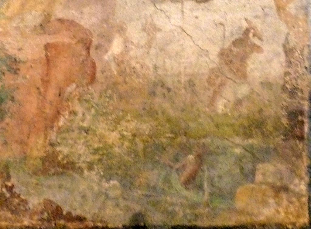 V.2.10 Pompeii. May 2010. Detail from wall painting from east wall of room 9, cubiculum. 
Minerva’s helmeted figure, partly obliterated, sits, piping, on a rock near a shrine. Her shield is by her side.
She is looking at an attendant nymph who emerges from the water holding a large mirror which is tilted slightly upwards.
A figure with a cornucopia sits watching nearby.
Now in Naples Archaeological Museum. Inventory number 120626.
