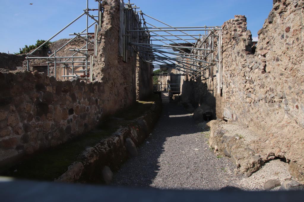 Vicolo dei Balconi, Pompeii. October 2022. Looking north from junction with Via di Nola.
V.2.20 Pompeii is centre left, lit by sunlight. V.2.21 is on the left behind V.2.20, in line with the ramp in the roadway.  
Photo courtesy of Klaus Heese.