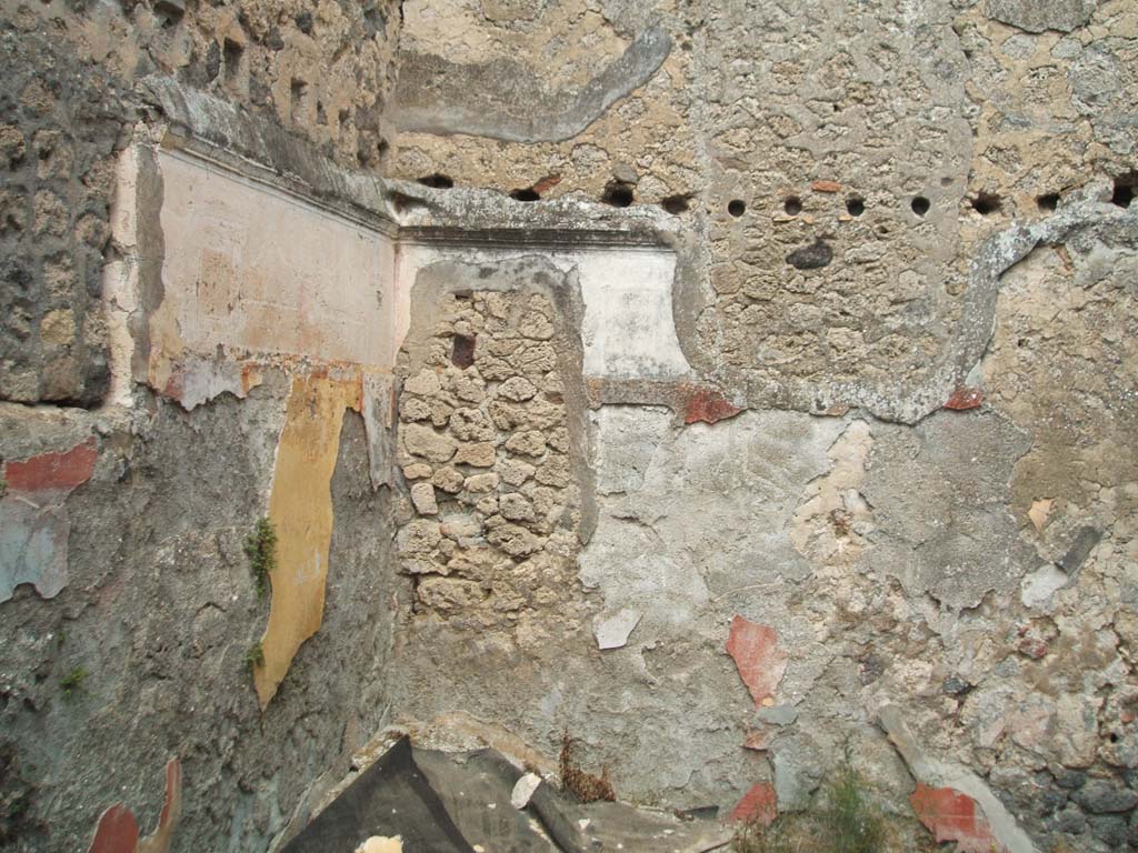 V.2.d Pompeii. May 2005. Room “m”, looking towards the north-east corner of the triclinium.
The blocked window in north wall overlooked V.2.i and was blocked after excavation.
The holes for the support beams of an upper room can be seen in the walls.
This upper room would have been reached by the masonry steps against the east wall in the previous photos.  
In the remains of the yellow panel of the north wall, just visible in the centre would have been a painting of monochrome green glass vases on a yellow background.
According to PPM, the middle zone of the north wall was decorated with yellow side panels, and a red panel in the centre edged with “carpet” border and separated by black compartments with painted cane/reeds. On the white upper zone would have been architecture and painted garlands together with a stucco cornice.
Not a lot remains of the decoration of the east wall.