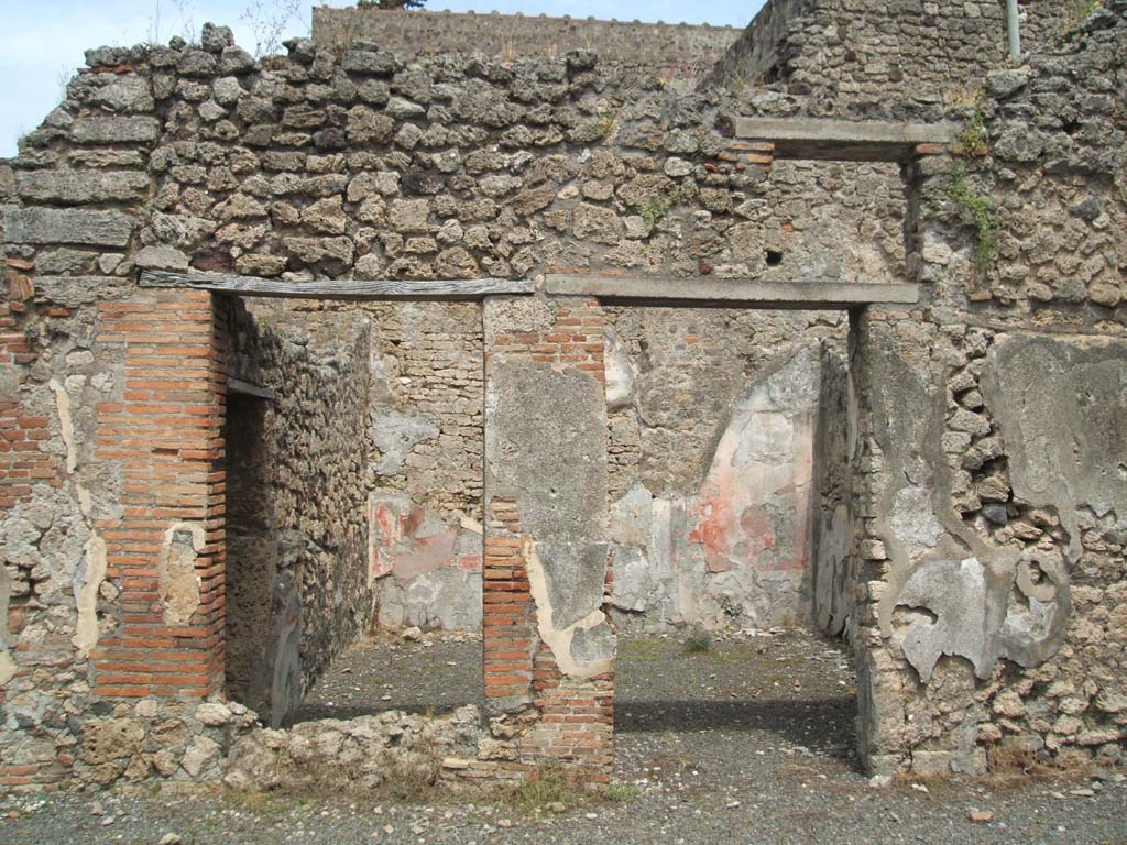 V.2.g Pompeii. May 2005. Room ‘k’ on the east of the atrium, with remains of painted plaster.
According to NdS, this room which had a window onto the atrium, was decorated with opus signinum flooring.
The walls were divided into red and white panels with a white frieze, and black dado.
In the central white panel of each wall was a painting.
When excavated, only the one on the east wall remained, and the lower edge of the one on the south wall. 
According to Sogliano, from what he could see and described from the painting on the south wall, he thought it had probably been a representation of Perseus freeing Andromeda.
In each of the panels was a flying figure, painted on a red background. 
Also seen on the south wall on the red plaster was a graffito of the following numerals:
XXIIIII
XXIIIII
XXXI
See Notizie degli Scavi di Antichità, 1896, (p.420)