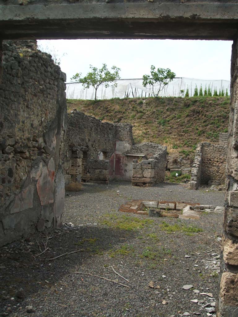 V.2.g Pompeii. May 2005. Looking north through room ‘m’ the tablinum, across atrium to entrance. 
According to NdS, the tablinum was on the south side of the atrium between the cubiculum ‘h’ on the left, and the corridor ‘L’ on the right.
The tablinum had a window in its south wall which led onto the north portico of the garden.
It had opus signinum flooring, and walls decorated with red panels except for the central ones which were yellow.
In the middle of all of the panels were small rectangular squares with the usual circular crudely painted landscapes.
At the foot of the east wall was a recess for a bed, and a travertine one-legged support was found there.
Found on the red plaster of the dado of the west door-jamb, on the side pointing towards the entrance, (on the left of this photo), was the graffito:
CAESARIS
See Notizie degli Scavi di Antichità, 1896, (p.420-21).