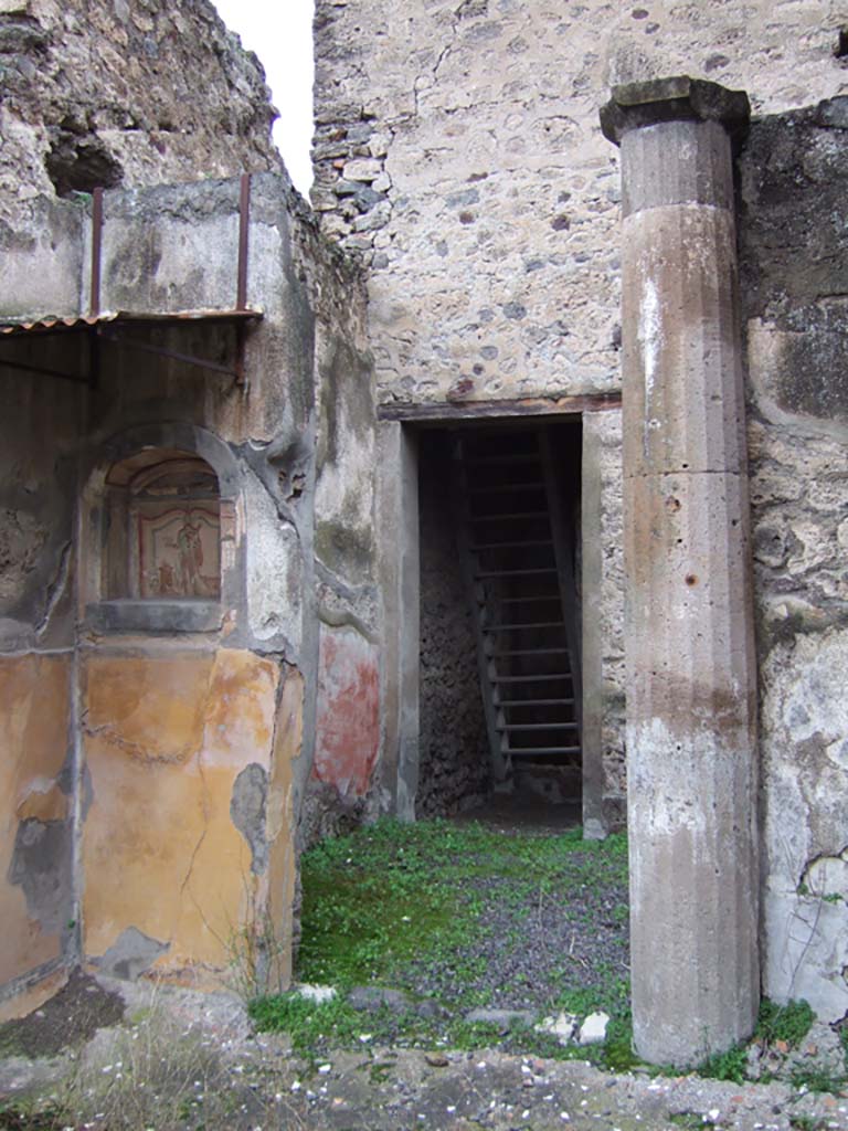 V.2.h Pompeii. December 2005. 
Looking north to doorway from walkway ‘k’, across area ‘h’, to room ‘e’, the corridor, with wooden reconstructed stairs to the upper cenacolo. 
According to NdS, corridor ‘e’ had a threshold of travertine and walls covered with a rustic white plaster.
In the north-west corner of room ‘e’ was a low masonry block, probably the beginning of an ascending stairway.
At the south end of the corridor was a doorway (seen above) leading into area ‘h’, which also had doorways to the tablinum ‘f’, to room ‘i’ a cubiculum, to room ‘l’ triclinium, and doorway to walkway ‘k’ (above) leading to the garden, room ‘n’. 
The small garden ‘n’ was preceded by a walkway ‘k’ protected by a roof, which projected from the roof, which covered room ‘h’.
This walkway had a floor of flagstones, littered with chunks or flakes of marble, and did not show any other decoration other than a high yellow dado on the west wall and in the north-west corner.
See Notizie degli Scavi di Antichità, 1896, (p.423) which refers to walkway ‘h’, across area ‘f’, to corridor ‘c’, with wooden stairs, cubiculum ‘i’, triclinium ’g’, garden ‘l’. 
In the north-west corner of walkway ‘h’, on the north side of the garden, was a lararium niche and column.
According to Boyce, in the garden was found a cylindrical altar of terracotta, around which a serpent coiled, its head raised above the top.
See Boyce G. K., 1937. Corpus of the Lararia of Pompeii. Rome: MAAR 14. (p.36, note 1).