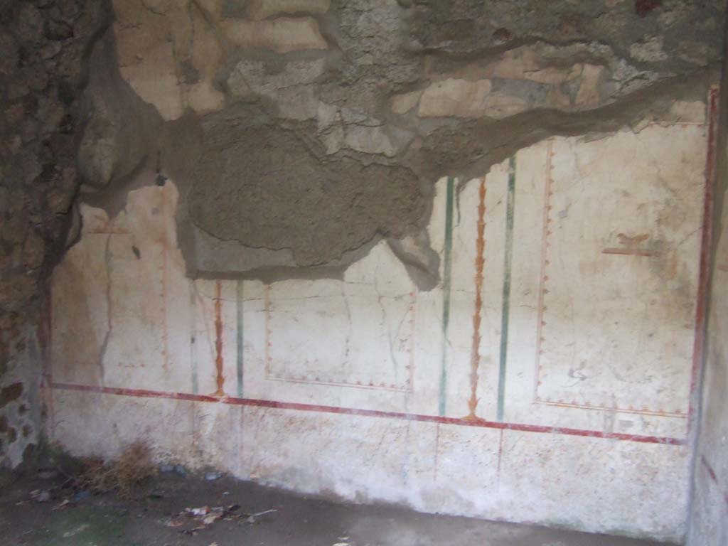 V.2.h Pompeii. December 2005. Cubiculum ‘b’, remains of painted decoration on the north wall.
According to Spano, when excavated the walls of this room were described as having a complete white background.
Each wall was split into three rectangular compartments, separated by yellow candelabra and green bands, and a bird in the centre of each division. 
The upper frieze was almost entirely destroyed but was probably decorated with the usual bands and arabesques.
The lower part of the wall was decorated with squares of small specks of various colours, imitating marble.
The floor was of mortar with numerous marble stones set into it.
Found in this room on September 28th 1907 were three bone cylinders perhaps furniture hinges, together with three nails, a ring, and a type of small ferrule, all in bronze.
See Spano in Notizie di Scavi di Antichità, 1910, p.329 where it is referred to as ‘c’.