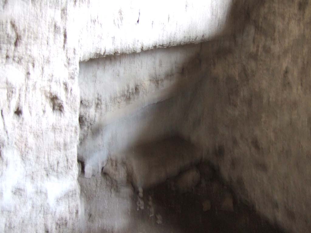 V.2.h Pompeii. December 2005. Kitchen ‘p’, recess in north-west corner.
According to Spano, a square window with preserved grating was found in the north wall.
Along the north wall, but perhaps at night only, may have been put a small bed.
In the west part of the north wall can be seen the characteristic hollowed recess destined to contain one of the ends of the bed. 
See Spano in Notizie degli Scavi di Antichità, 1910, p.330 where the kitchen is referred to as ‘d’.
According to NdS, (1896), the west side (on the left) of the atrium was devoid of rooms.
On the east side, there was one small area with the possible clue of a staircase ascending to the rooms above the entrance fauces and the two adjacent rooms. 
See Notizie degli Scavi di Antichità, 1896, (p.422).
In NdS, (1910), further excavation had discovered a doorway to the kitchen on the east side of the atrium.
According to the newer discovery, it was then thought that the room above the cubiculum on the right of the fauces was accessible from above a room in the adjoining house. 
The kitchen and the room from the house next door would have been in communication in ancient times.
In the left half of the east wall of the kitchen, a bricked-up wall/doorway could be seen. 
A latrine was then constructed in front of the new bricked up wall, with the hearth on its right.
See Notizie degli Scavi di Antichità, 1910, (p.329-330) where the cubiculum on the west is referred to as ‘c’ and the east one as ‘b’.