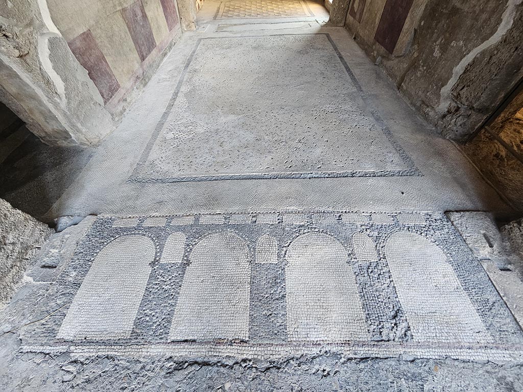 V.2.i Pompeii. November 2024. Room 14, looking west across flooring of antecamera of apodyterium or dressing room.
The threshold is made of a red and white mosaic showing a series of arches of an aqueduct. Photo courtesy of Annette Haug.